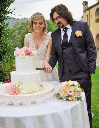 Sara e Davide durante il taglio della torta; l'abito da sposa componibile di Sara illumina la scena con i suoi riflessi glitter.